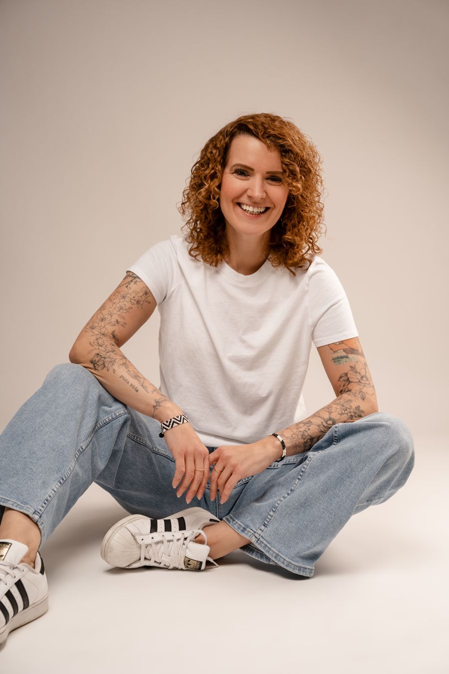 Annika Schmitz im weißen T-Shirt, im Schneidersitz auf dem Boden, lachend